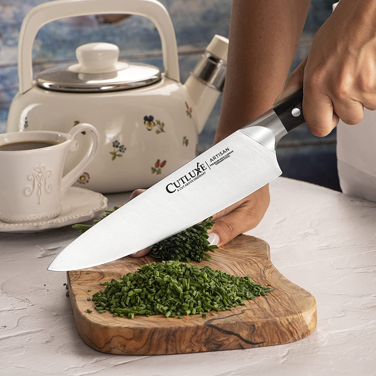 Product image 3 of 9: Chef slicing fresh chives with a Cutluxe Artisan chef knife on wooden cutting board, kitchen scene