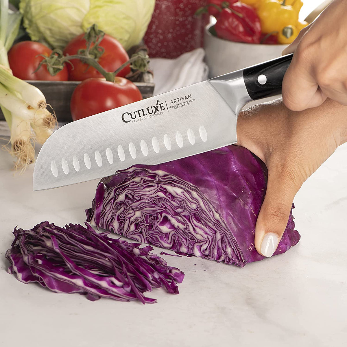Product image 4 of 8: Cutluxe Artisan chef knife slicing red cabbage on marble countertop with fresh vegetables