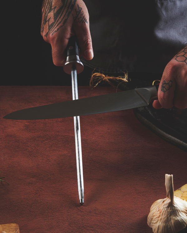 Chef sharpening a high-quality kitchen knife on a wooden surface with garlic nearby