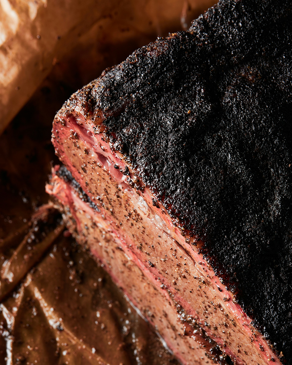 Smoked brisket with charred crust and juicy pink interior, seasoned with pepper