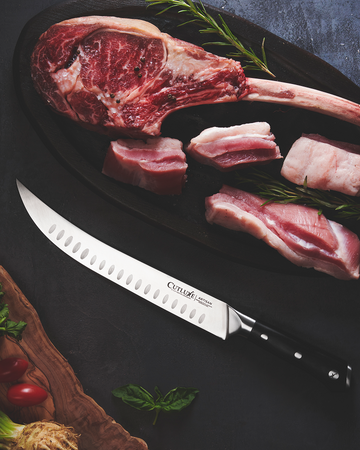 Cutluxe artisan knife slicing raw steak and pork on dark board with herbs
